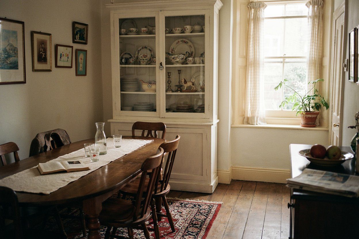A dining room with a table, chairs, a loaded china cabinet and framed pictures still hanging, each carrying a small price sticker
