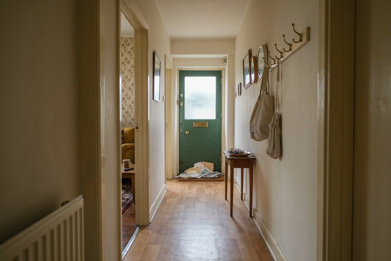 The hallway and front room of an ordinary British house still fully furnished, with a stack of unopened post on the mat